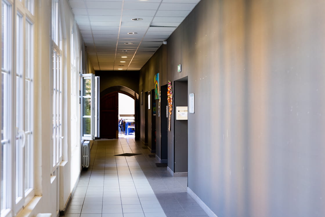 Couloir sobre et lumineux avec de grandes fenêtres sur le mur de gauche et des portes qui donnent accès aux salles de classe sur la droite.